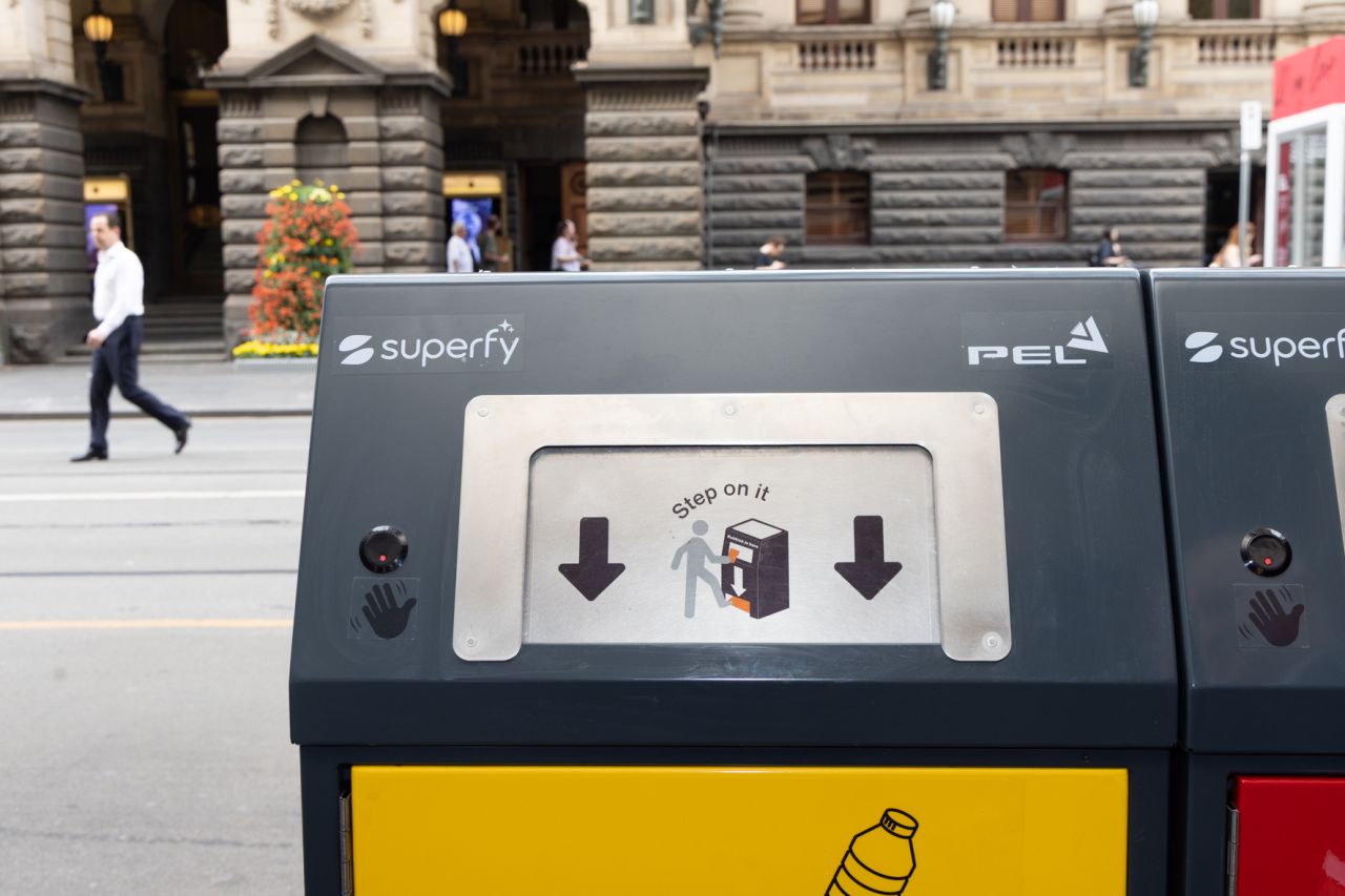 Yellow recycling and red waste PEL solar compacting bins on a Melbourne CBD footpath, with a man passing behind